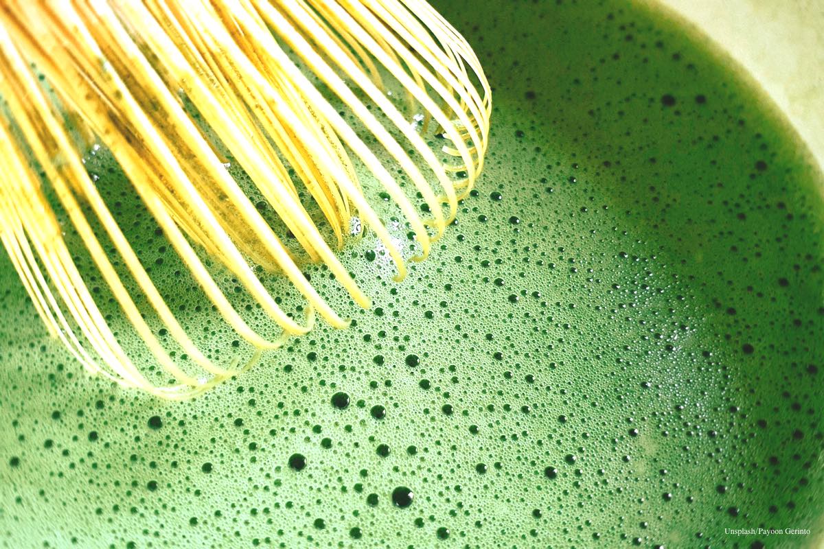 A close-up of a bamboo chasen whisk creating vibrant green froth in a bowl of ceremonial grade matcha.