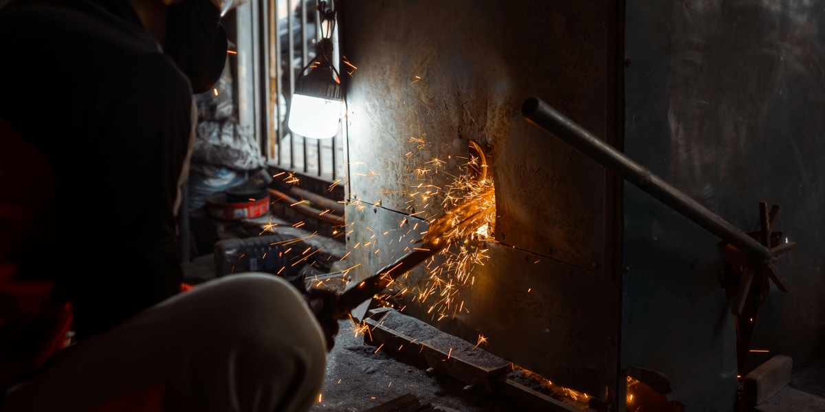 A Japanese master blacksmith hand-forging premium steel for hair scissors, with orange sparks flying from the anvil.
