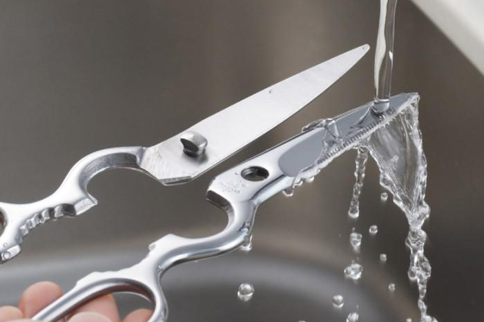 The two blades of a disassembled Japanese kitchen scissor being rinsed under running water.